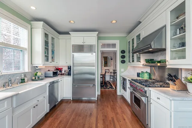 a kitchen with stainless steel appliances granite countertop a refrigerator a sink dishwasher a stove and white countertops with wooden floor