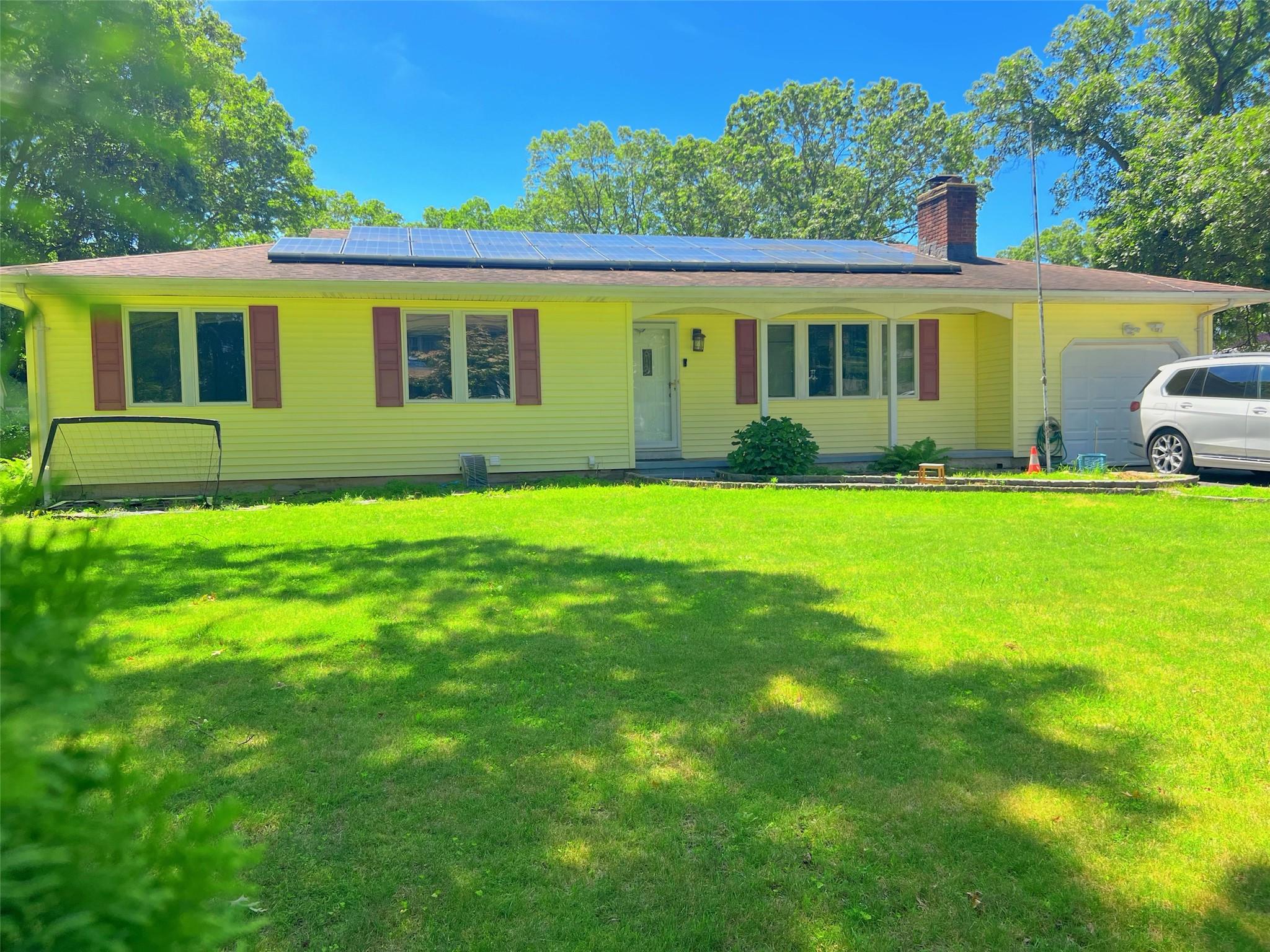 Ranch-style house with an attached garage, a chimney, a front yard, and solar panels