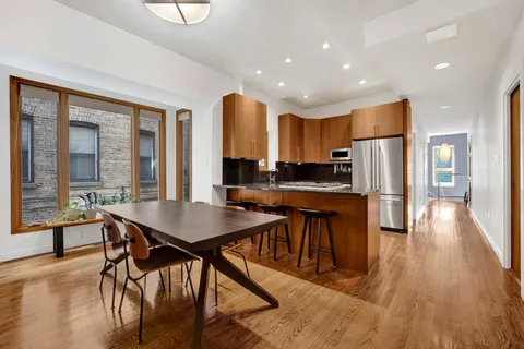 a kitchen with stainless steel appliances granite countertop a stove a refrigerator a sink a dining table and chairs with wooden floor