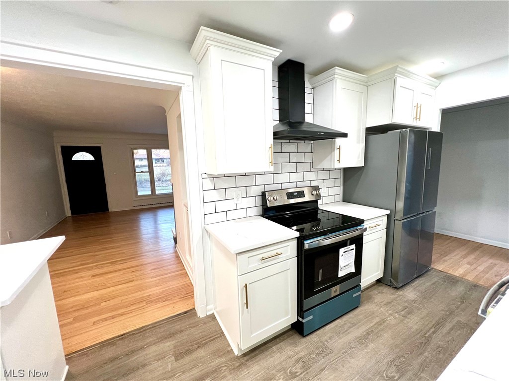 7687 Ragall Parkway Cleveland, OH 44130 - Photo 9 of 37 Kitchen featuring wall chimney exhaust hood, stainless steel range with electric cooktop, white cabinetry, backsplash, and light hardwood / wood-style floors
