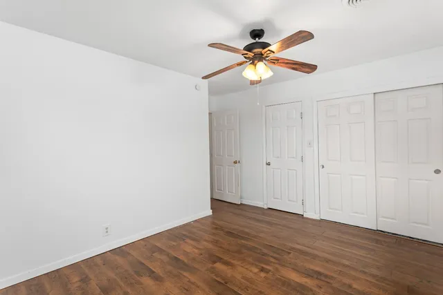 a view of an empty room with wooden floor and a ceiling fan
