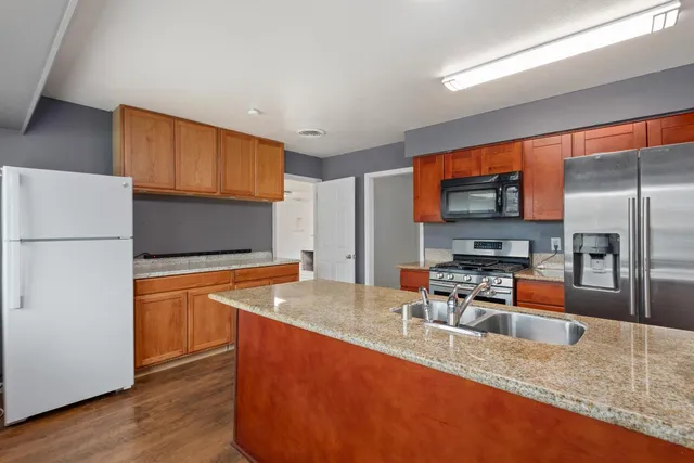 a kitchen with stainless steel appliances granite countertop a refrigerator a stove and a sink with wooden floor