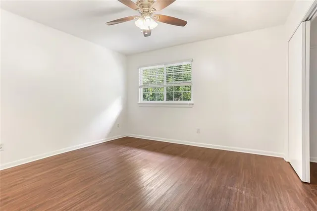 an empty room with wooden floor chandelier fan and windows