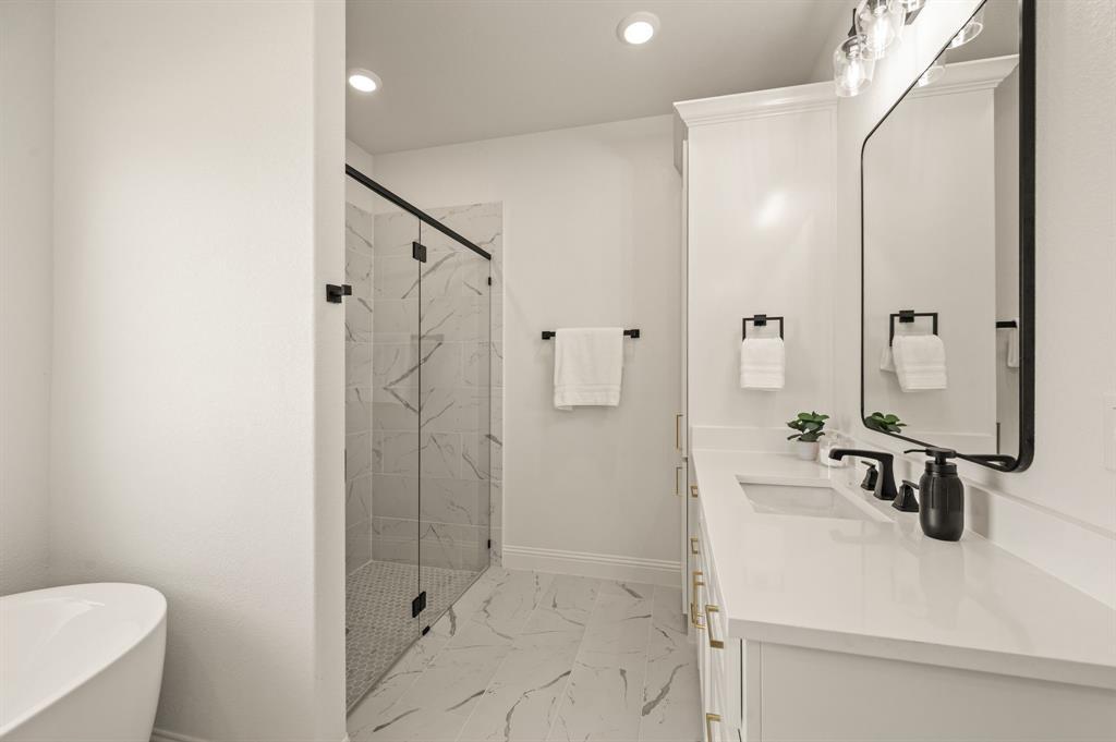 2705 Gospel Road Tolar, TX 76476 - Photo 20 of 36 Modern bathroom featuring a frameless glass shower enclosure with patterned tile, a freestanding soaking tub, a single vanity with a white countertop and undermount sink, a rectangular mirror with a black frame, and recessed lighting