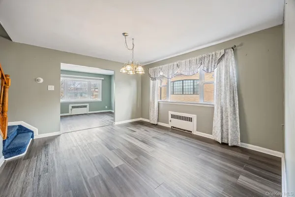 an empty room with wooden floor chandelier and windows