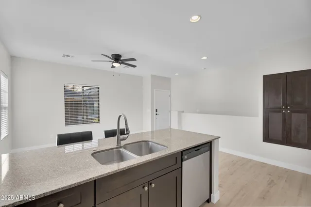 a living room with stainless steel appliances kitchen island granite countertop a stove top oven a sink a dining table and chairs with wooden floor