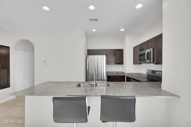 a kitchen with stainless steel appliances kitchen island granite countertop a refrigerator and a stove top oven with wooden floor