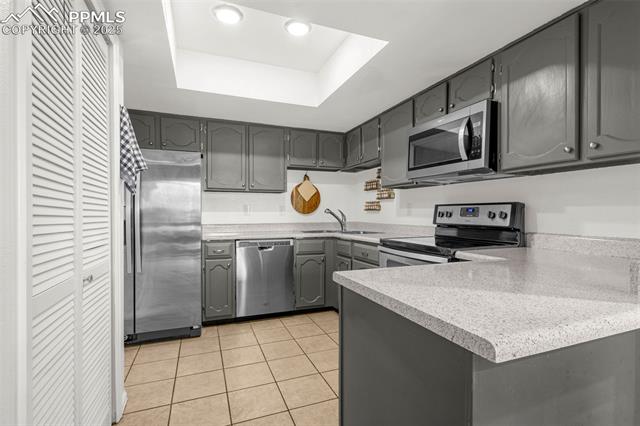 4990 Castledown Road Colorado Springs, CO 80917 - Photo 8 of 37 Kitchen featuring gray cabinetry, a tray ceiling, a sink, and appliances with stainless steel finishes