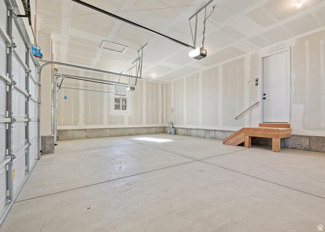 11214 South Easy Bee Road, Unit 270 South Jordan, UT 84009 - Photo 15 of 31 Expansive two-car garage featuring a concrete floor, automatic door opener system, a side access door with wood steps and handrail, a single frosted window, and a utility access panel