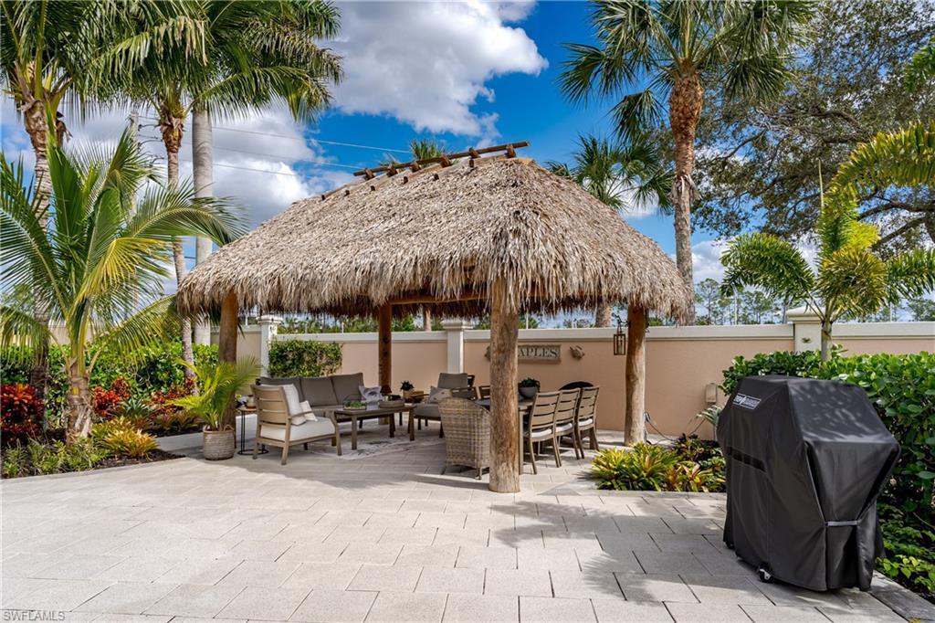 13595 Snook Circle Naples, FL 34114 - Photo 8 of 35 a view of a patio with table and chairs under an umbrella with a fire pit and palm trees
