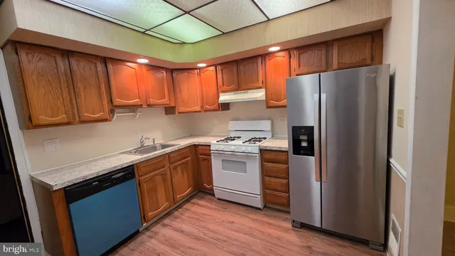 a kitchen with stainless steel appliances granite countertop a refrigerator a sink dishwasher a stove with wooden cabinets and floor