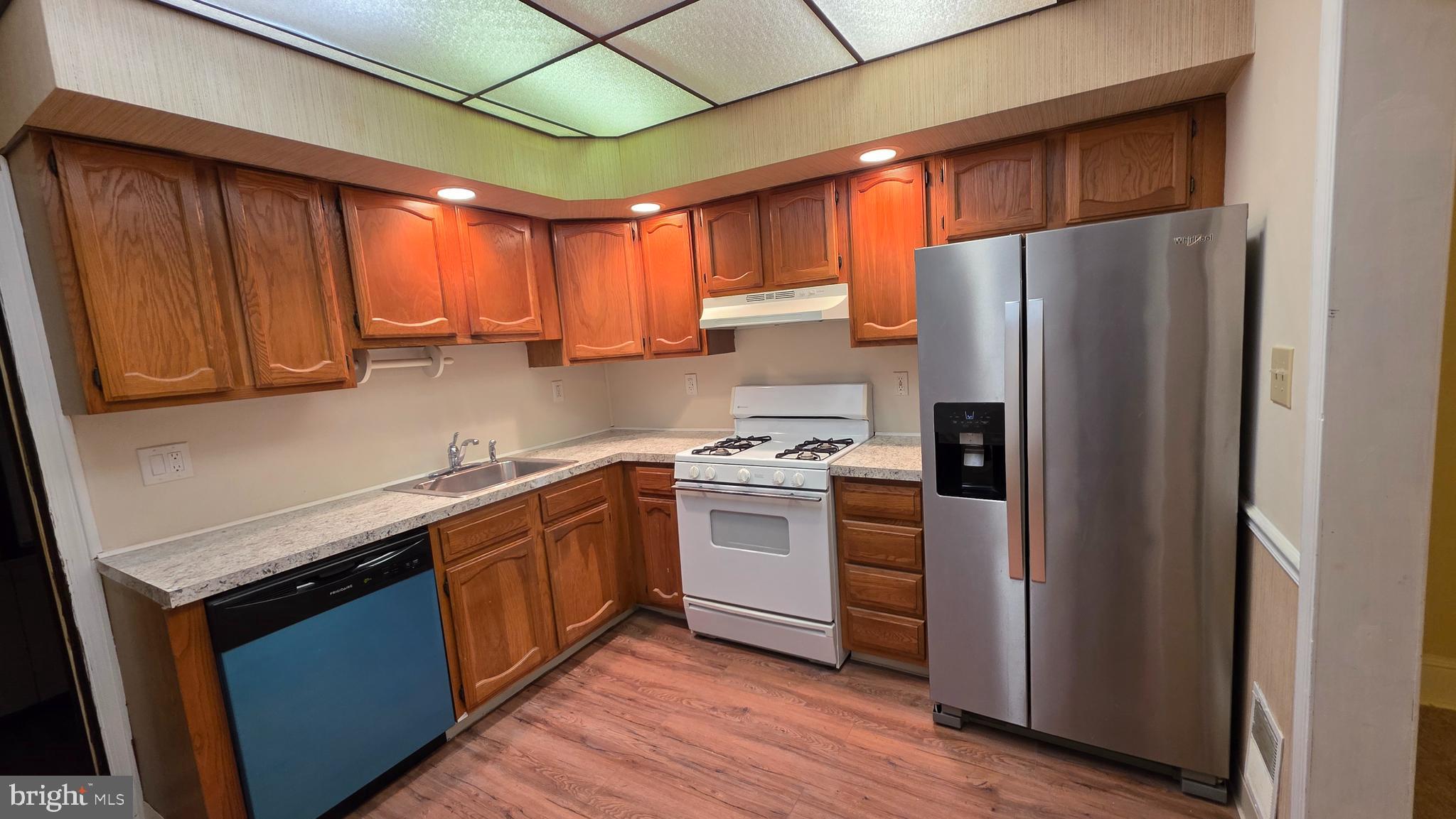 a kitchen with stainless steel appliances granite countertop a refrigerator a sink dishwasher a stove with wooden cabinets and floor