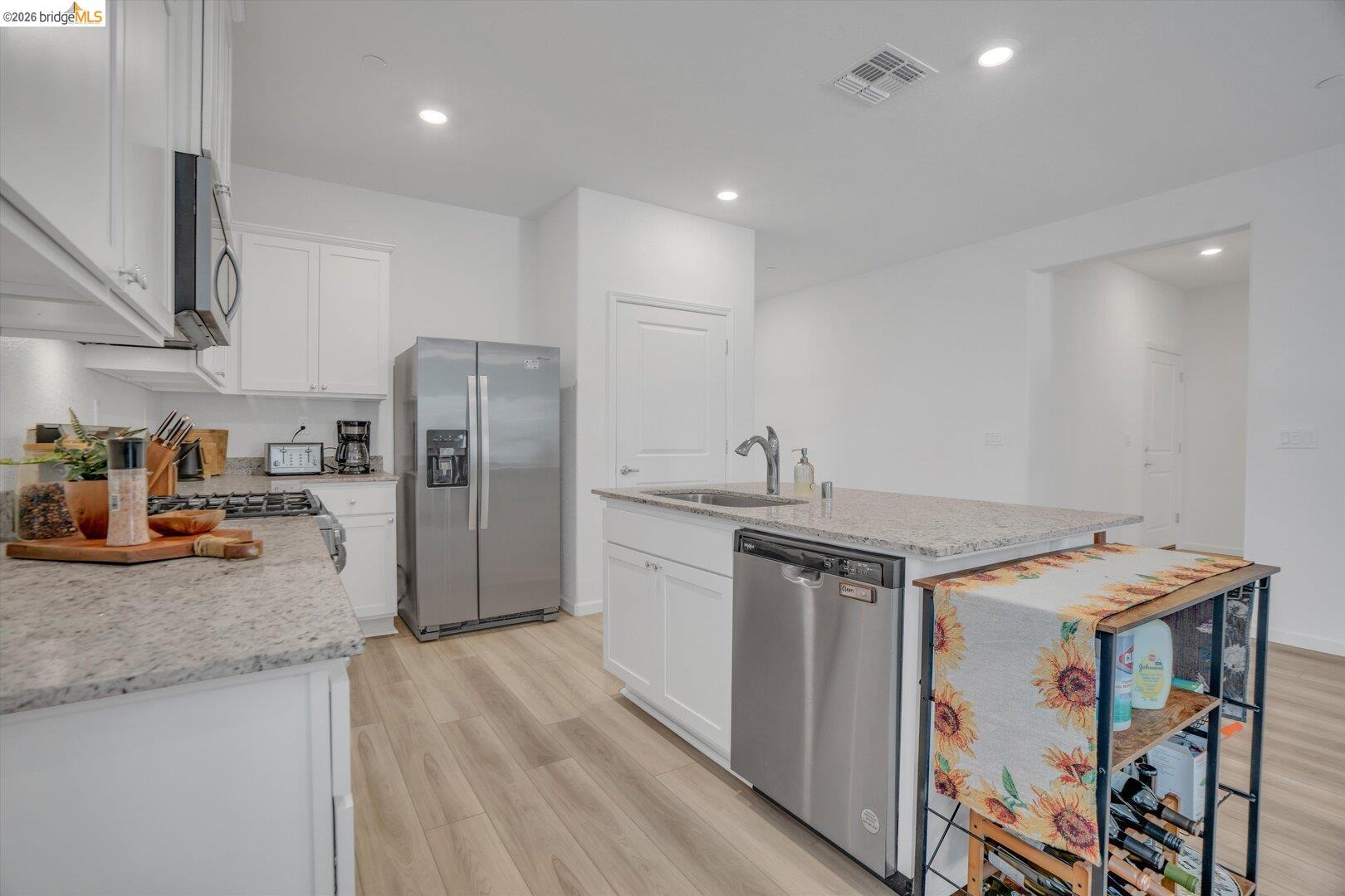 4463 Canada Way Rio Vista, CA 94571 - Photo 18 of 36 kitchen featuring light wood finished floors, stainless steel appliances, an island with sink, light stone countertops, and white cabinets