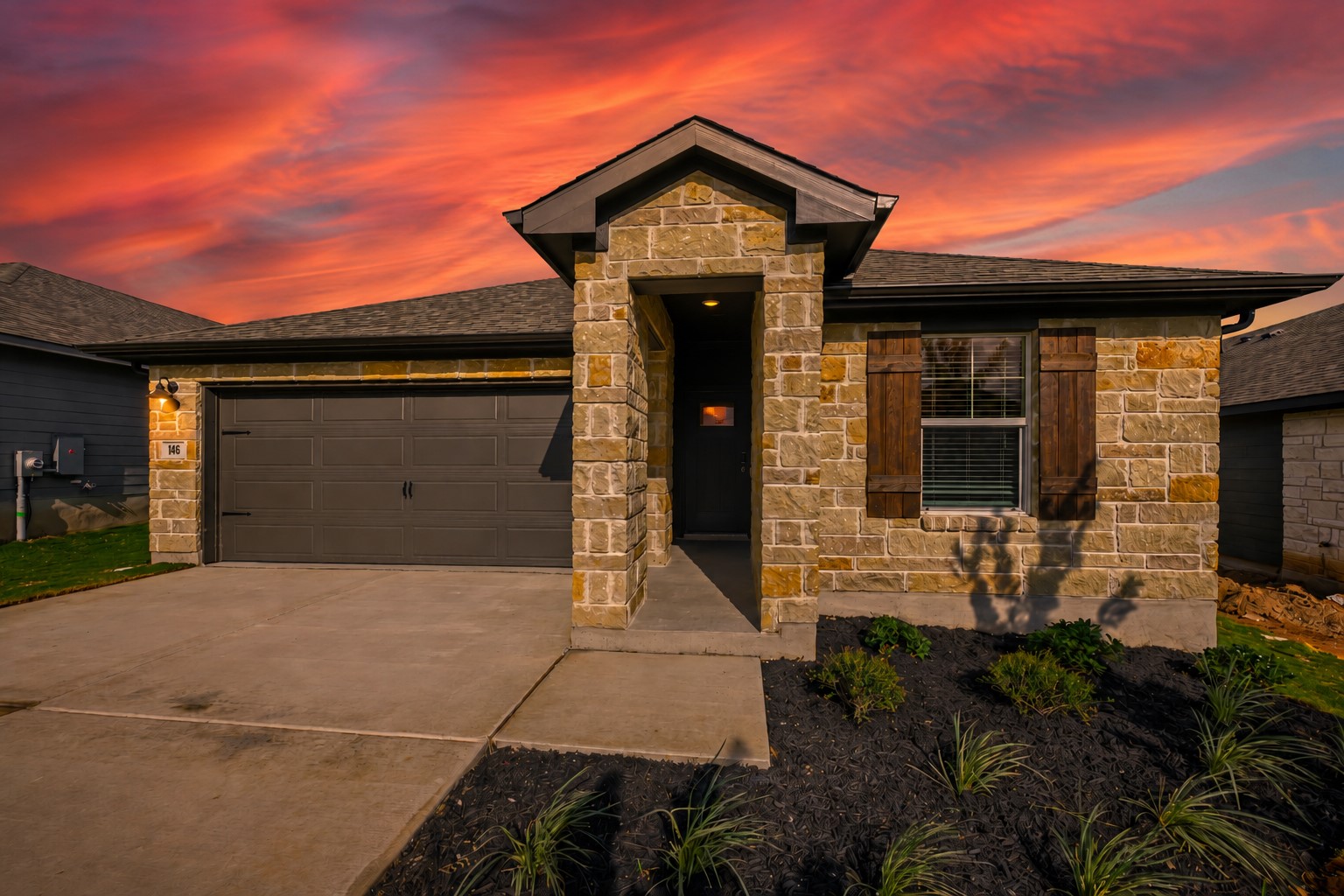 146 Diablo Rim Terrace Dripping Springs, TX 78620 - Photo 1 of 32 A welcoming stone facade with a prominent front entrance and attached garage under a fiery sky.