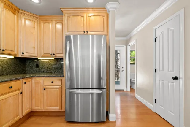 a kitchen with stainless steel appliances granite countertop a refrigerator a sink and white cabinets with wooden floor