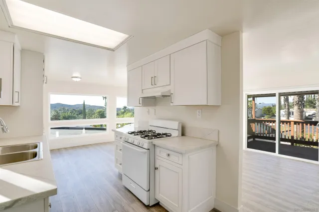 a kitchen with stainless steel appliances a white stove top oven and white cabinets next to a window