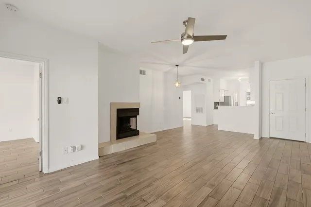 an empty room with wooden floor ceiling fan and kitchen view