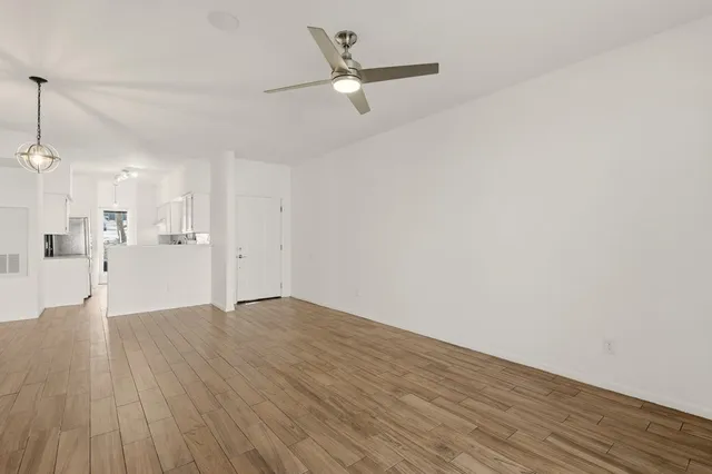 a view of an empty room with wooden floor and a ceiling fan