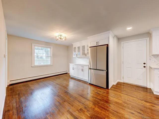 a view of an empty room with wooden floor and a kitchen