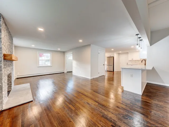 a view of empty room with wooden floor and kitchen view
