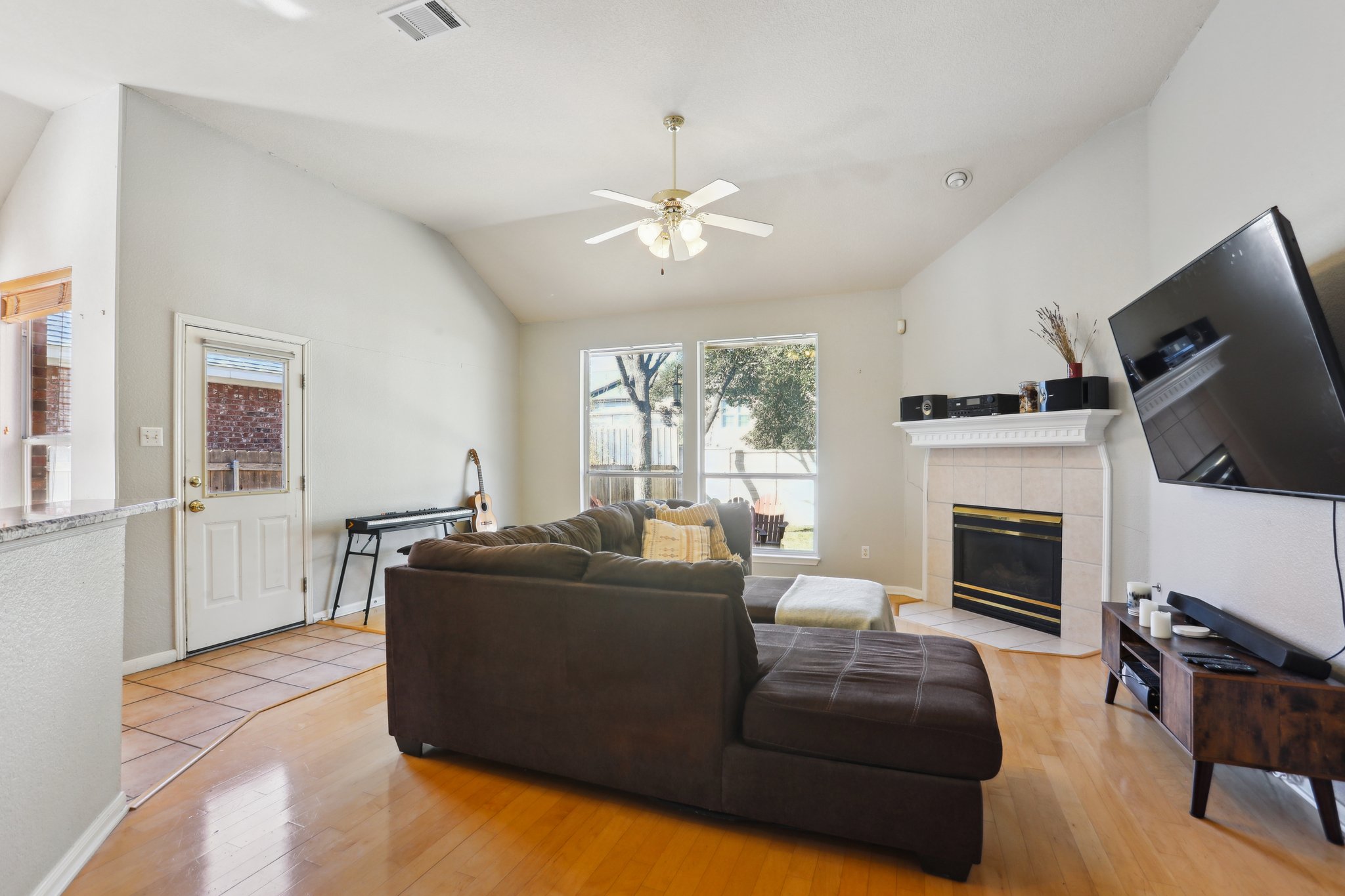 13541 Anarosa Loop Austin, TX 78727 - Photo 5 of 27 Living area featuring vaulted ceilings, wood-finish flooring, a tiled fireplace with a mantel, and multiple windows