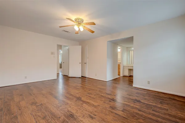 a view of an empty room with wooden floor and a ceiling fan