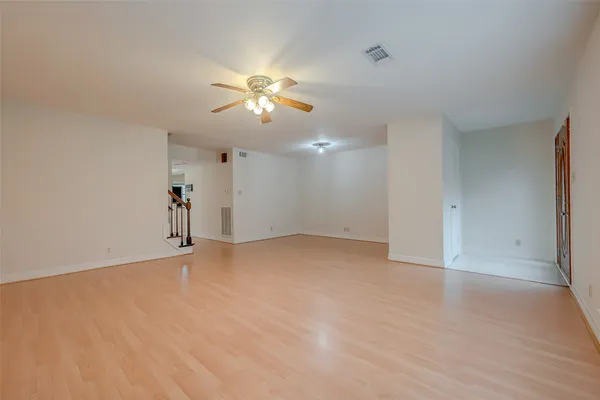 a view of an empty room with chandelier fan and wooden floor