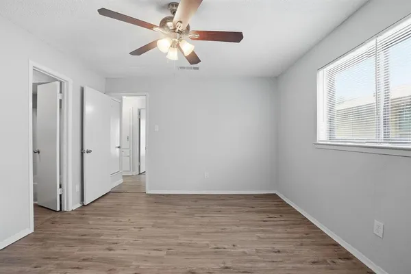 an empty room with wooden floor fan and windows