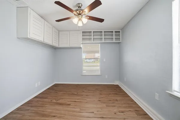 an empty room with wooden floor fan and windows