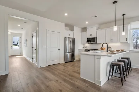 a kitchen with stainless steel appliances granite countertop a refrigerator a sink dishwasher a stove and white cabinets with wooden floor