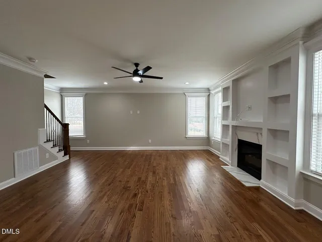 an empty room with wooden floor fireplace and windows