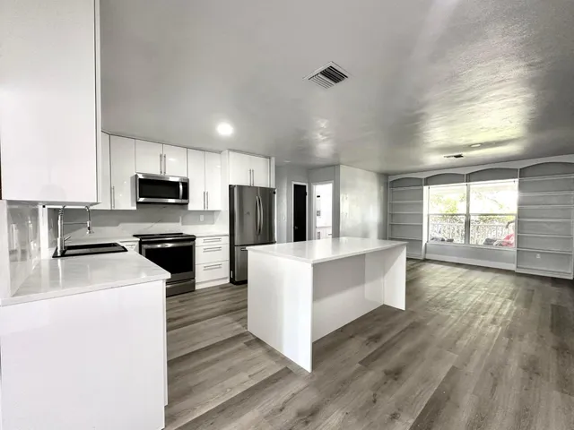 a large kitchen with a center island wooden floor stainless steel appliances and windows