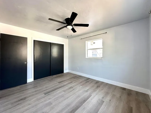 a view of an empty room with wooden floor and a ceiling fan