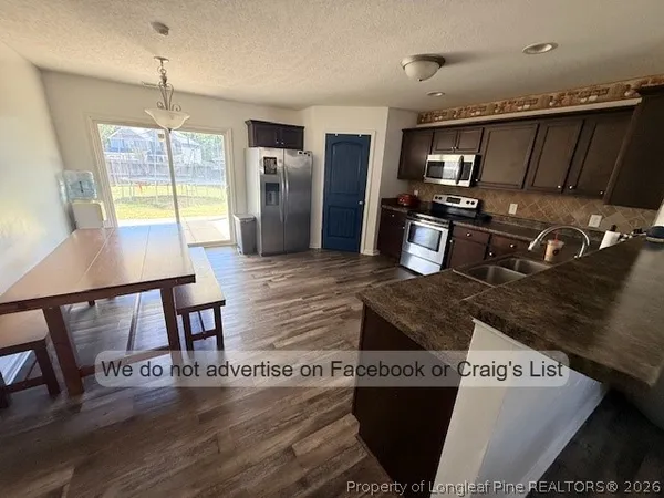 a kitchen with stainless steel appliances granite countertop a refrigerator a stove and a dining table with wooden floor