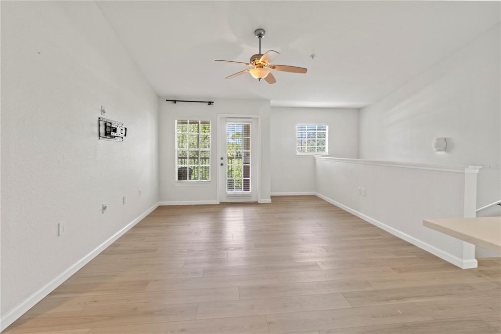 8827 Manor Loop, Unit 201 Lakewood Ranch, FL 34202 - Photo 12 of 39 an empty room with wooden floor chandelier fan and windows