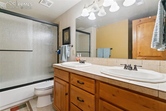 5470 Roundup Ridge Road Colorado Springs, CO 80908 - Photo 14 of 21 Full bathroom featuring double sink vanity, shower / bath combination with glass door, backsplash, tile floors, and toilet