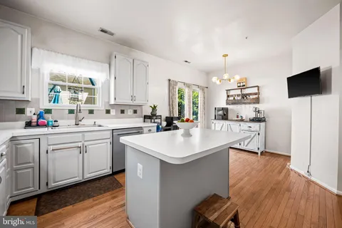 a kitchen with stainless steel appliances kitchen island a sink a stove a refrigerator and white cabinets with wooden floor