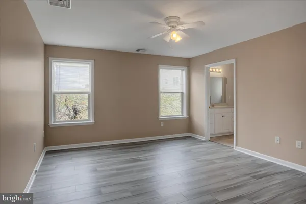 an empty room with wooden floor ceiling fan and windows