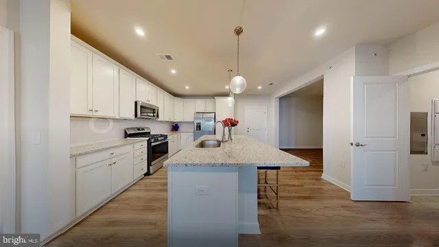 a kitchen with stainless steel appliances kitchen island granite countertop a refrigerator a sink dishwasher and white cabinets with wooden floor