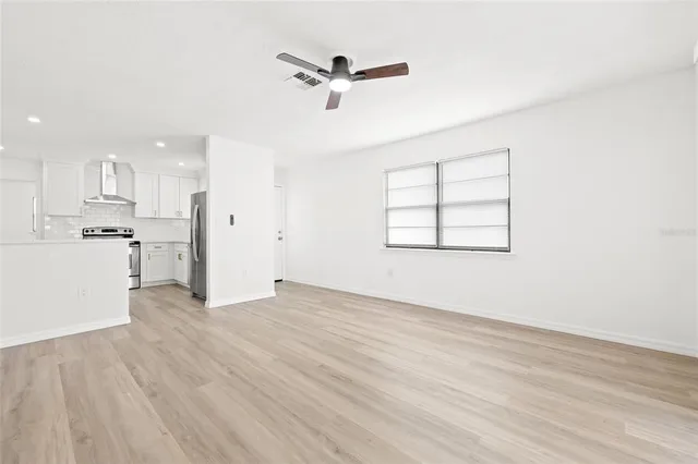 an empty room with wooden floor a ceiling fan and kitchen view