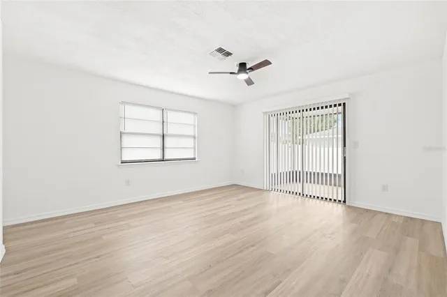 an empty room with wooden floor ceiling fan and windows