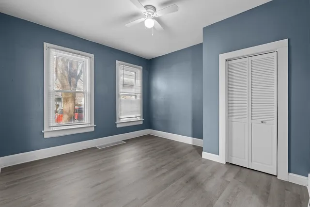 an empty room with wooden floor chandelier fan and windows