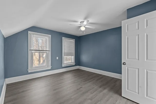 an empty room with wooden floor chandelier fan and windows