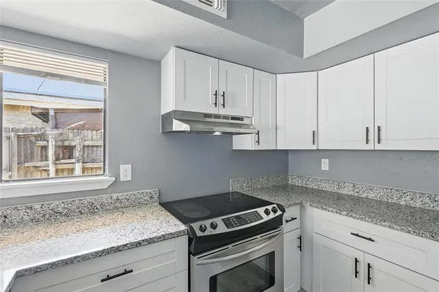a kitchen with granite countertop stainless steel appliances white cabinets granite counter tops and a wooden floors