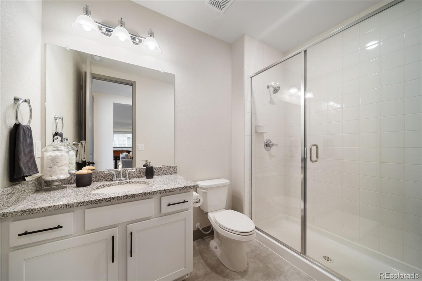 6465 Barnstead Drive Castle Pines, CO 80108 - Photo 44 of 50 a bathroom with a granite countertop sink toilet a mirror a vanity and shower