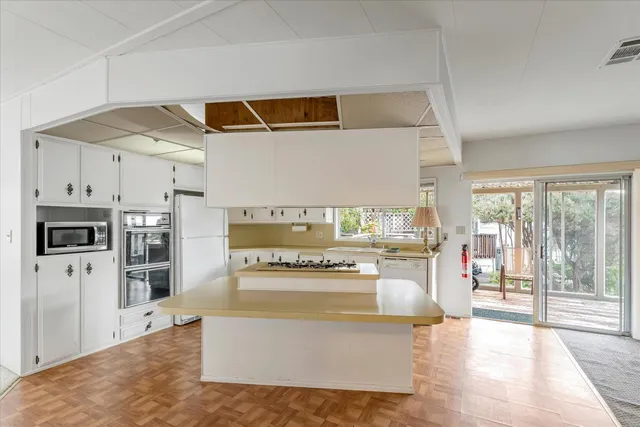 a kitchen with stainless steel appliances kitchen island wooden cabinets a stove a sink dishwasher and a dining table with wooden floor