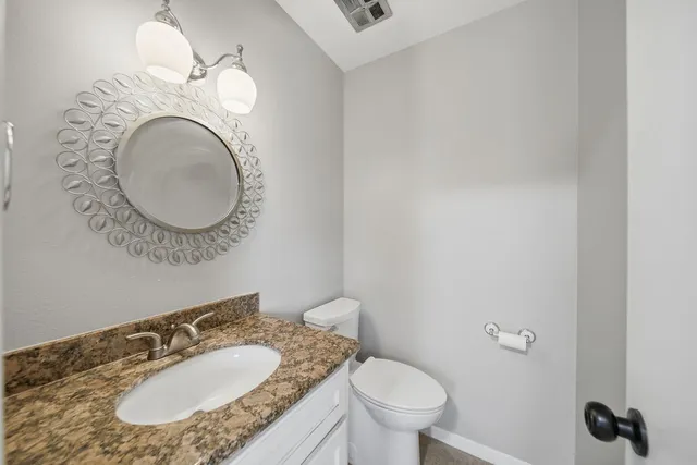 a bathroom with a granite countertop toilet a sink and a mirror