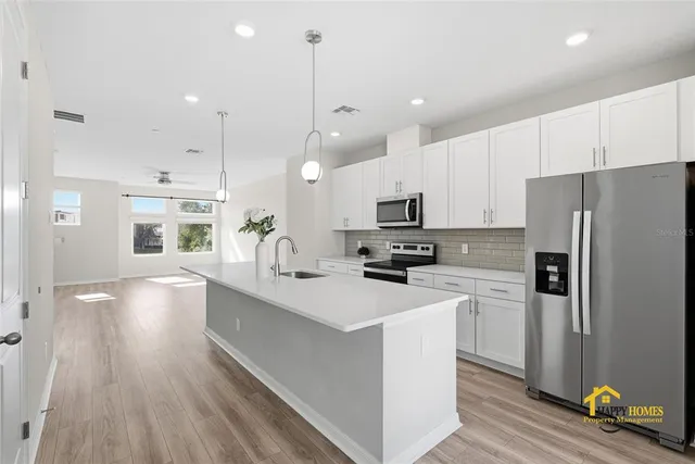 a kitchen with stainless steel appliances a refrigerator a sink dishwasher a stove top oven a refrigerator with white cabinets and wooden floor