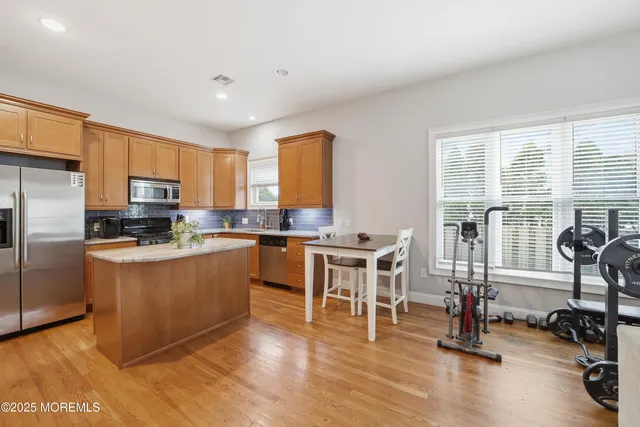 a kitchen with stainless steel appliances granite countertop a stove top oven a refrigerator a dining table and chairs with wooden floor