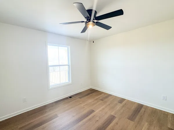 an empty room with wooden floor ceiling fan and windows